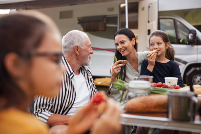 An image of three generations of a family eating together while camping