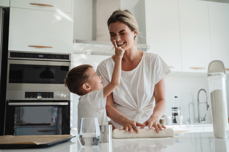 Mother and young son kneading dough together in bright modern kitchen sharing happy moment