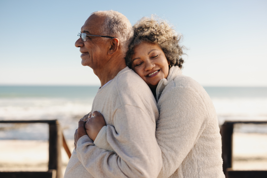 An image of a retired Canadian couple hugging at a beach, thankful for health insurance as seniors and retirees