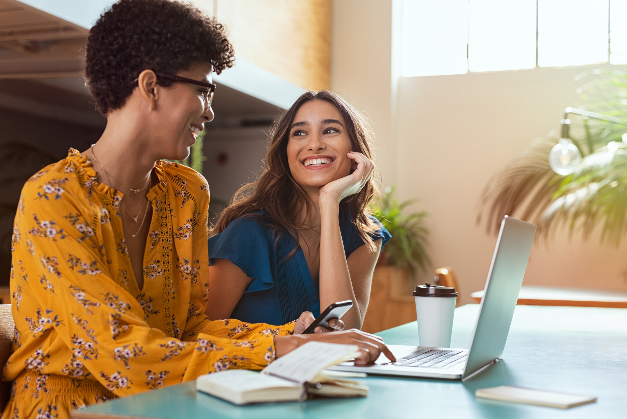 An image of two women looking at a phone and laptop comparing health insurance options