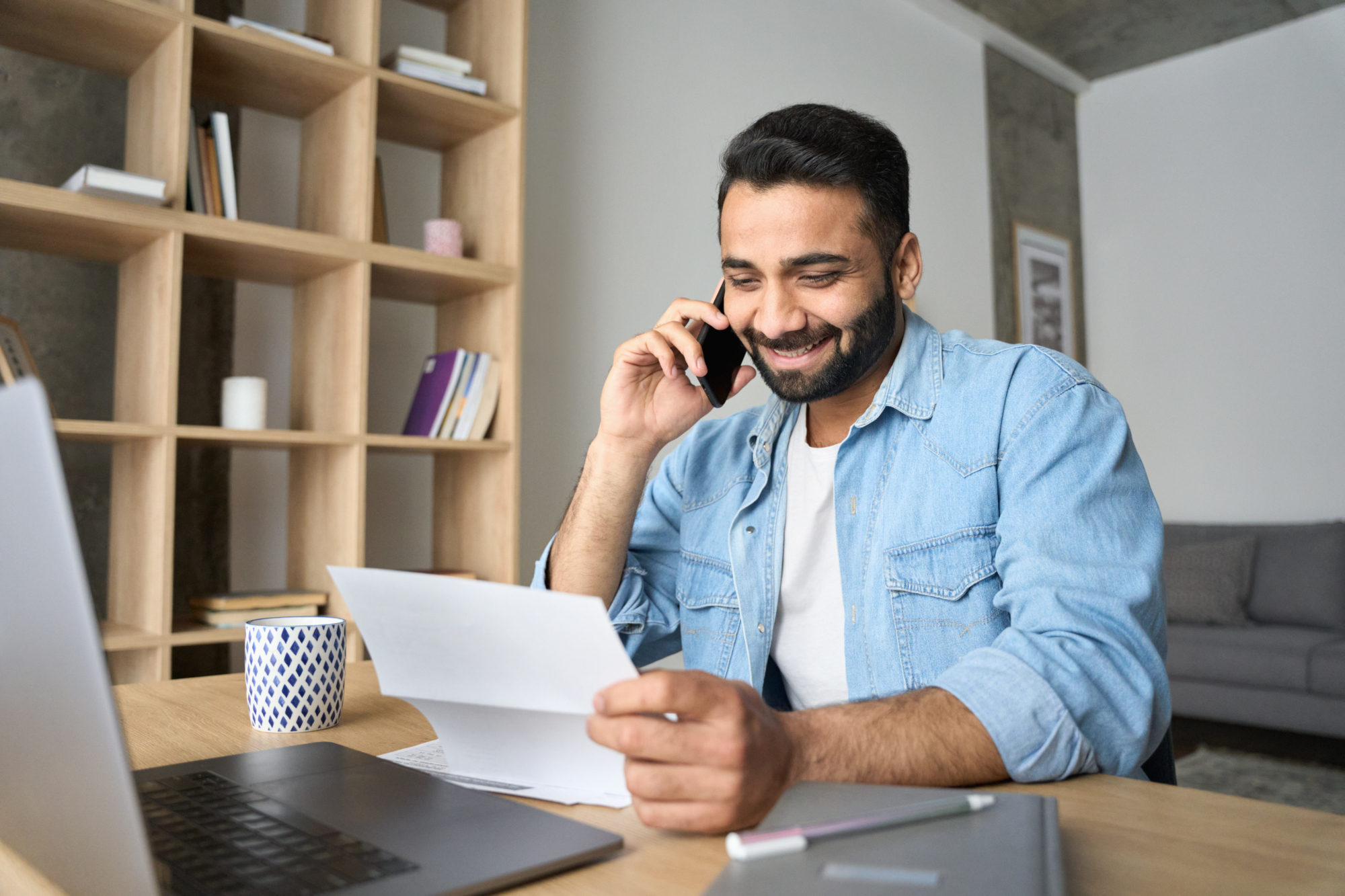 An image of a man at a desk with a laptop and a letter, talking on the phone about his individual health insurance